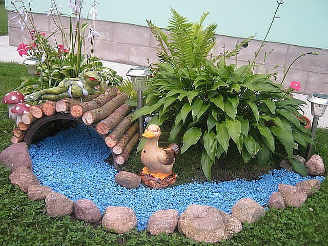 We decorate a dry stream: blue stones for water, duck figure, bridge, banks of stones and plants
