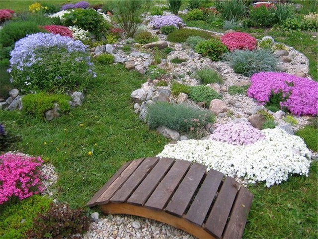 We decorate a dry stream of stones and flowers with a wooden bridge